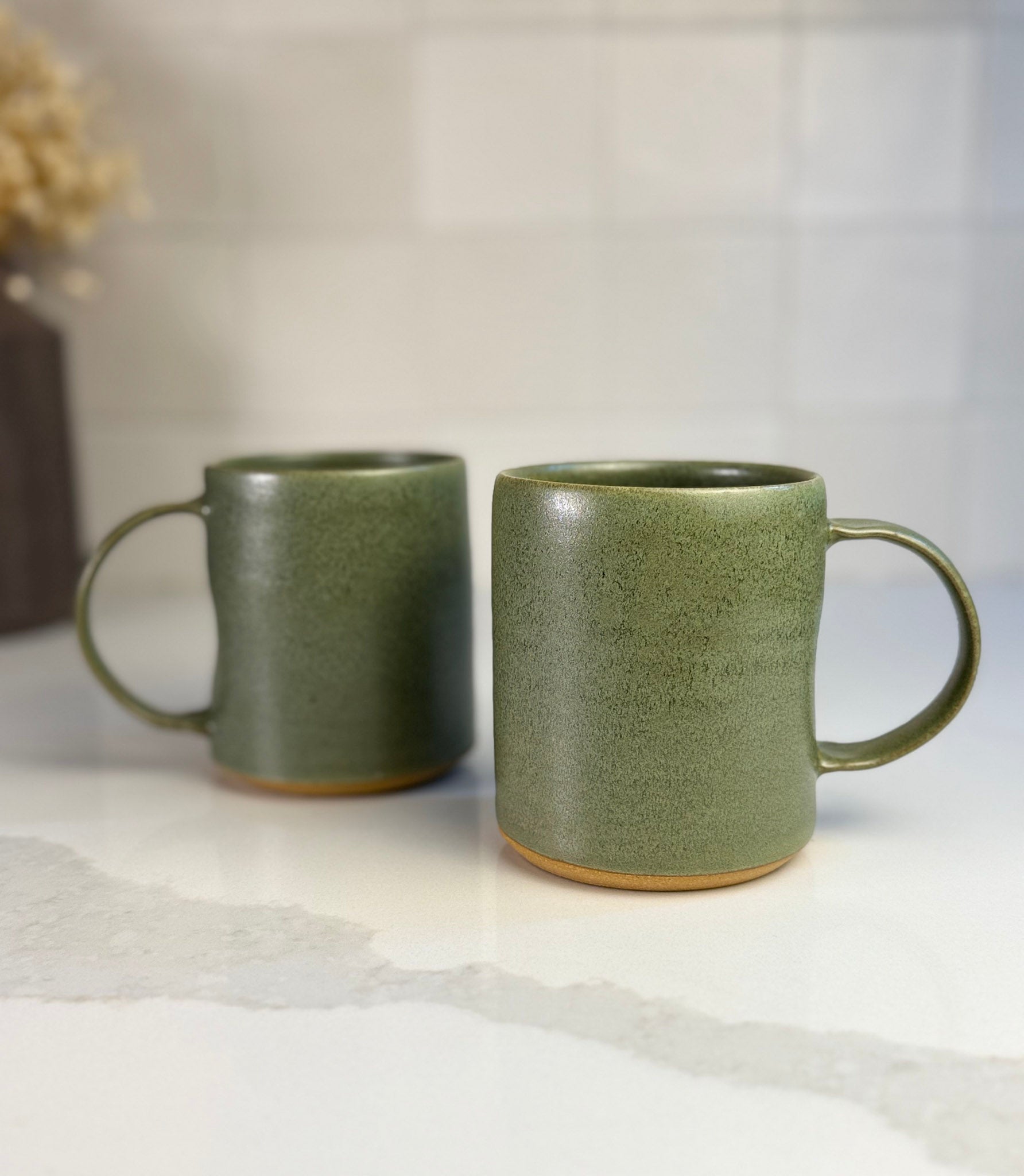 Two sage green mugs on a kitchen counter to show size and everyday use.