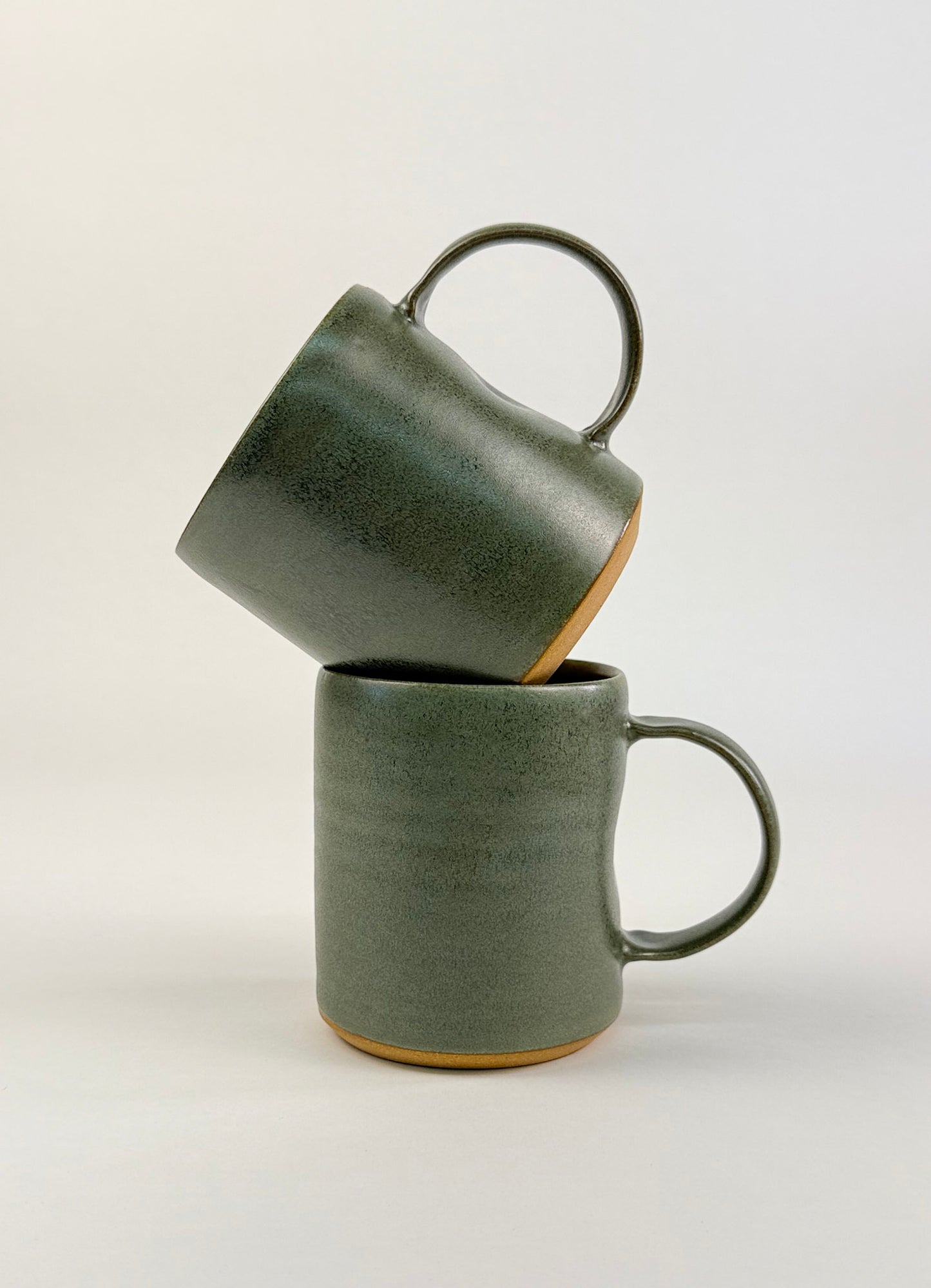 Two sage green ceramic mugs stacked on a clean white background showcasing artisan soap.