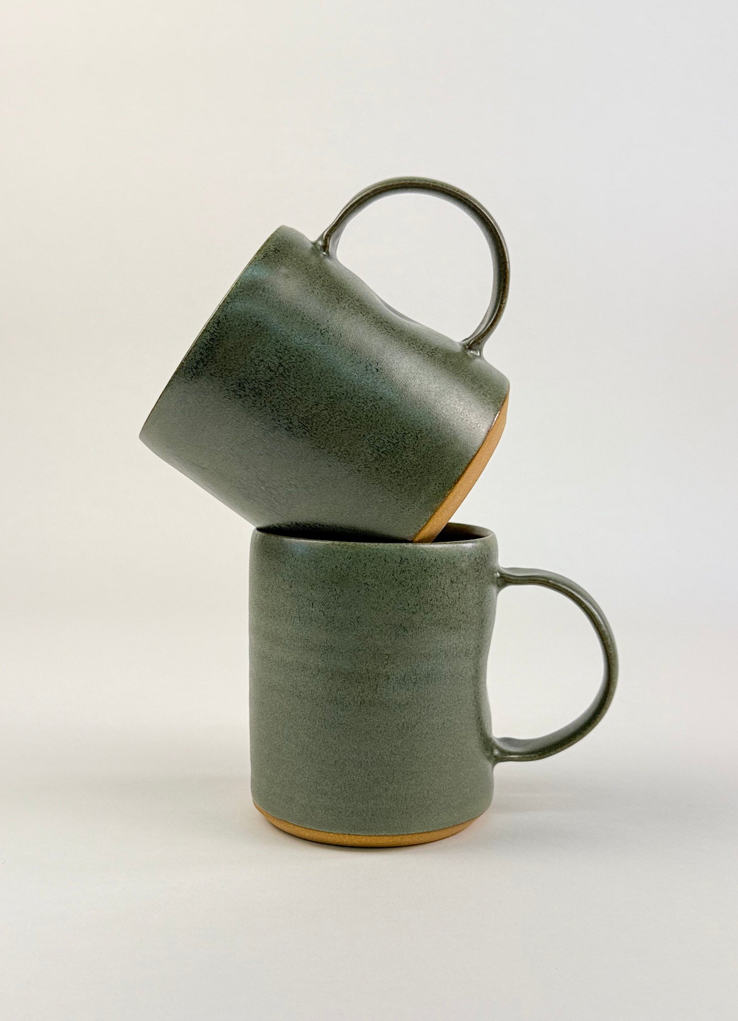 Two sage green ceramic mugs stacked on a clean white background showcasing artisan soap.